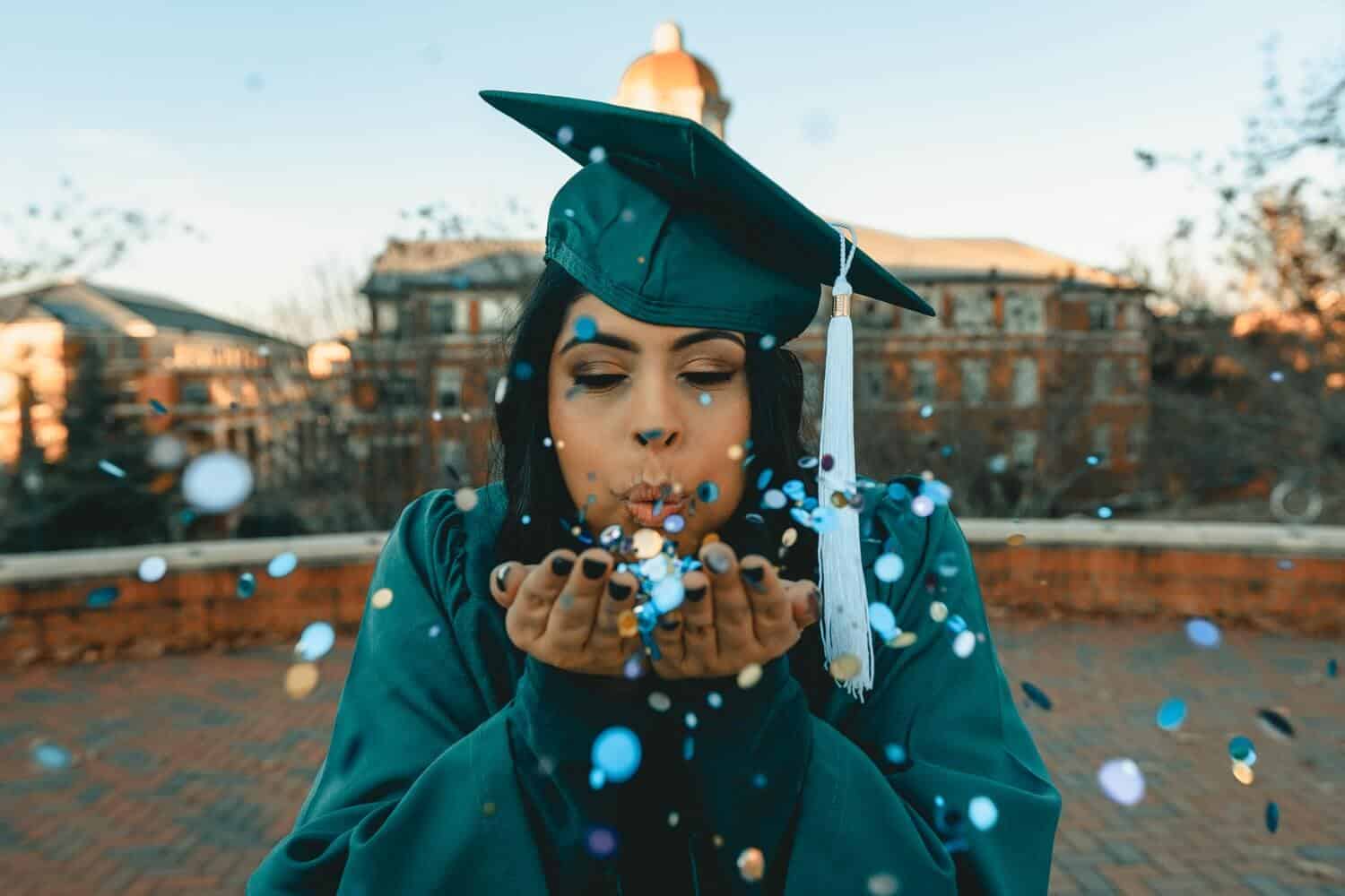 Image of a lady in a graduation gown blowing a kiss as a sign of celebration. Obviously, her college admission essay must have been accepted during her application to the school for her to be able to graduate.